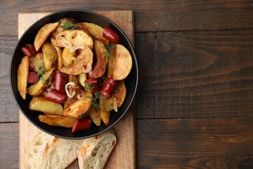 Delicious baked potato with thin dry smoked sausages in bowl and bread on wooden table, top view. Space for text