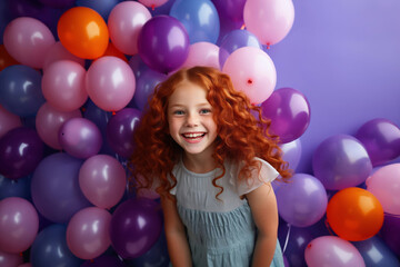 Fototapeta na wymiar Laughing little redhead curly girl with air balloons on violet background.