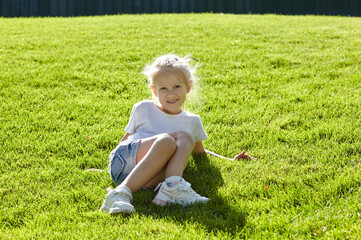Little girl sitting on the lawn in the summer city park. Childhood, leisure and people concept - happy child rest and have a good time