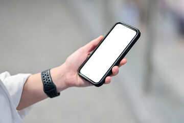 A close-up shot of a woman in casual clothes sitting in a cafe and using her smartphone. A white-screen smartphone mockup. people and wireless technology concepts