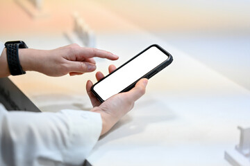 A close-up shot of a woman in casual clothes sitting in a cafe and using her smartphone. A white-screen smartphone mockup. people and wireless technology concepts