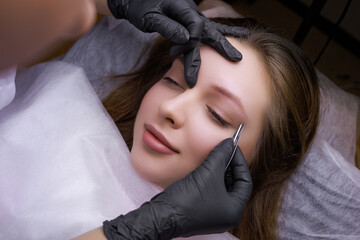 Top view of the model in which the master corrects eyebrows with tweezers before the procedure of...