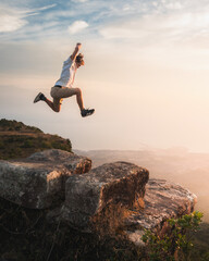 A man jumping on a rock at sunset at the top of a mountain