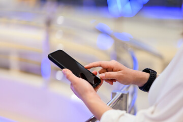 A cropped shot of an Asian woman using her smartphone, reading online articles, or responding to messages while sitting at a cafe in the city.