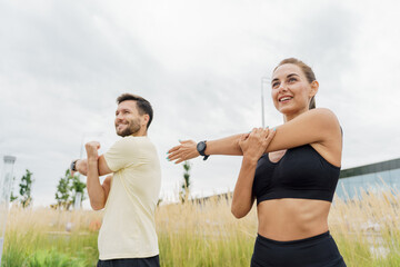 Smiling couple stretching outdoors, prepping for a workout in a grassy area.