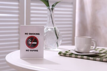 No Smoking No Vaping sign and cup of coffee on white table indoors