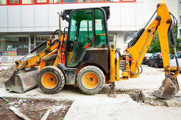A yellow tractor with front and rear hydraulic buckets stands on a construction site in the city.