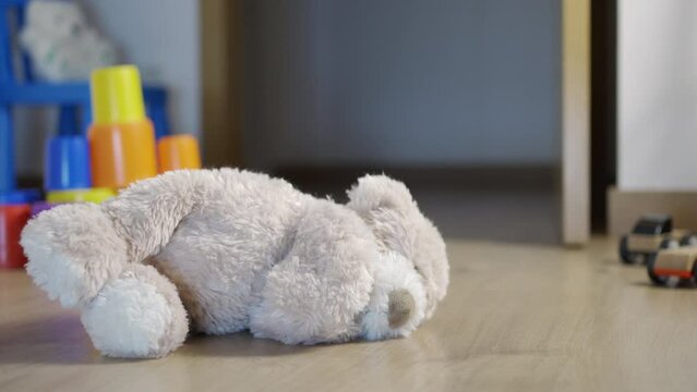 A teddy bear lying on the floor of a child's bedroom at night with an open door and other toys.Dolly shot.