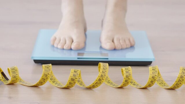 Closeup of tape measure and woman feet standing on weigh scales.Diet,weight loss and feet of a woman on a scale for body check,measure and balance to lose weight on the floor. Obesity concept