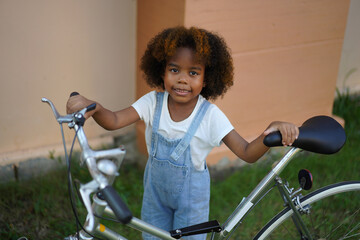 Obraz premium Young african girl smile stand confidently with hand on vintage bicycle, childhood adventure playing and joy, innocence and excitement for outdoor activities, healthy, family