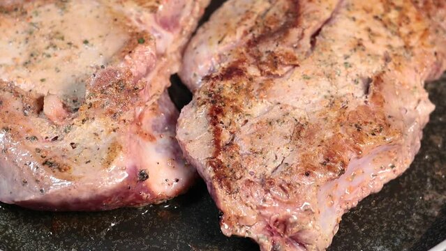 Delicious juicy pork steak is fried in a pan with smoke. Close up, slow motion footage.
