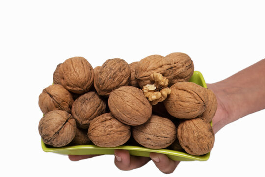 Handful of Fresh, Organic Walnuts in a Green Bowl, This image captures a hand holding a green bowl filled with whole, organic walnuts against clean, white background. The walnuts, with their textured