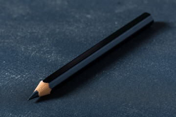 Close-up of a black pencil on a textured blue surface, ideal for design themes.