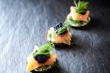 Smoked salmon canapes with cream cheese on black stone background. Close up.	