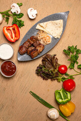 Juicy meat kebab with vegetables and herbs on a wooden table. view from above