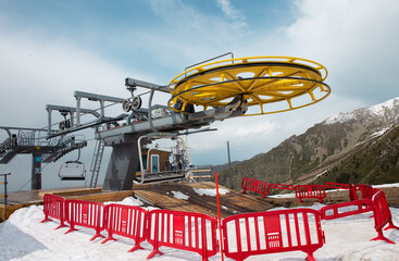 Yellow and gray ski lift wheel and tower with a blue sky and snow-capped mountains in the background