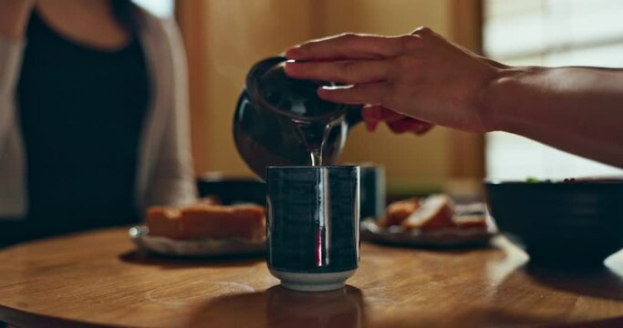 Person, hands and tea pot for pouring water at table for meal, Japanese tradition or eating together at home. Closeup of people with food, snack and drinking with chop sticks, mug or warm cup to drin