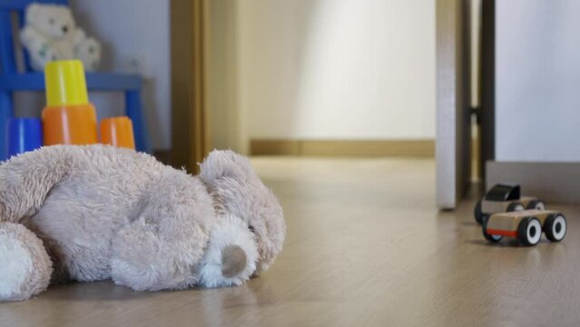 A classic brown teddy bear abandoned off the floor at night in a child's bedroom turning on the hallway light with an open door, as a man enters. Copy space.