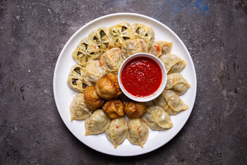 Uzbek samsas and manti with meat, pumpkin and greens on a plate with red sauce