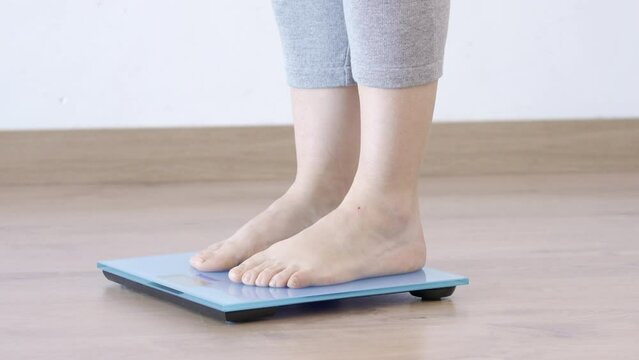 Close-up of a young woman weighing herself on a scale at home and throwing measuring tape on the blue scale.