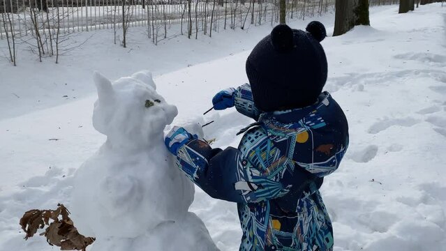 Playful child building snowcat in winter park, little boy making snowman Catherine Park, Pushkin, St. Petersburg.