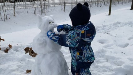Playful child building snowcat in winter park, little boy making snowman Catherine Park, Pushkin, St. Petersburg.