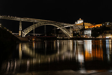 Dom Luis I bridge over Douro river and monastery of Serra do Pilar illuminated at night. Porto, Portugal. In first row some Rabelos, a type of boat traditionally used to transport wine barrels