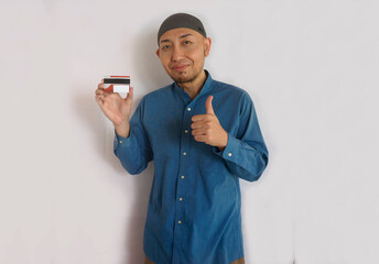 Happy Asian moslem man holding blank payment card for mockup and showing thumbs up