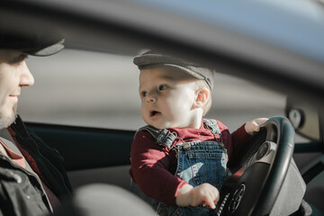 Young father with his little son driving car together. Child sit on dad laps, hold hands on steering wheel, bonding with his daddy