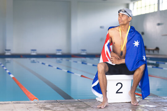 Swimmer wrapped in an Australian flag sits poolside with a medal, with copy space - Powered by Adobe