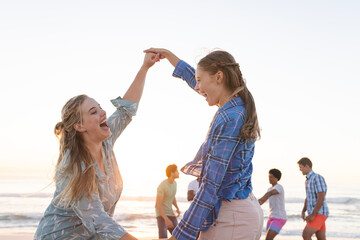 Two young Caucasian women dance on the beach at sunset