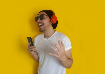 Young man singing his favorite song, using smartphone as microphone, wearing sunglasses, beanie hat...