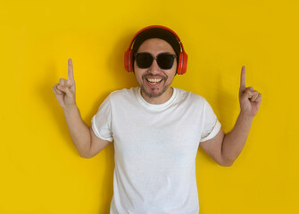 Young hipster man wearing headphones, beanie hat and sunglasses enjoy music over yellow background