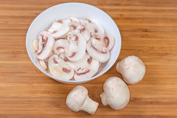 Raw sliced button mushrooms in bowl on wooden surface
