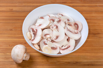 Raw sliced button mushrooms in bowl on wooden surface