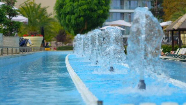Fountain splashing in resort pool with tropical backdrop in 4k slow motion 120fps