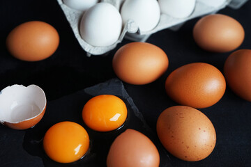Brown and white chicken eggs next to broken eggs on a dark background