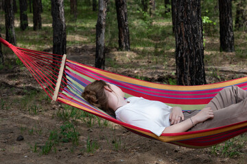 Obraz na płótnie Canvas Beautiful young woman relaxing in hammock in forest. Summer scenery, a beautiful morning in the bosom of nature. The girl admires the views and nature. Breathed fresh air. Beautiful morning light.
