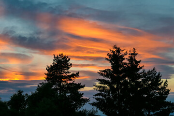 Sunset sky with clouds in the background and silhouette of trees in the foreground. The sky has vibrant orange pink color with clouds in the distance. Tranquil serene atmosphere on Petzen, Bleiburg