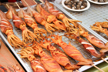 Grilled squid with sauce on skewers selling in thailand street food market with seafood