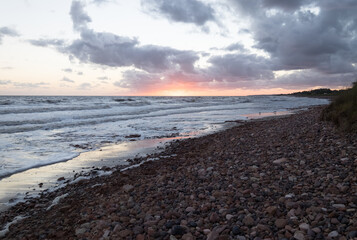 Fototapeta na wymiar sunset on a pebble beach, with the sun on the horizon and under a partly cloudy sky