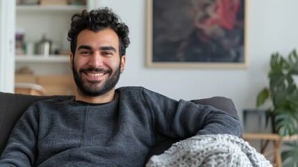 In this concept, a happy Middle Eastern guy enjoys a weekend break or weekend free time on a comfortable sofa in his living room. An image of a happy casual man enjoying weekend free time or a break - obrazy, fototapety, plakaty