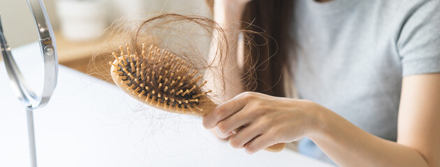 Problem hair, stressed beautiful asian young woman, girl hand holding comb show hairbrush with hair loss in brush after brushing fall near mirror at home. Health care, beauty with treatment concept.