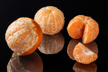 Three peeled mandarins beautifully reflected in mirrored background