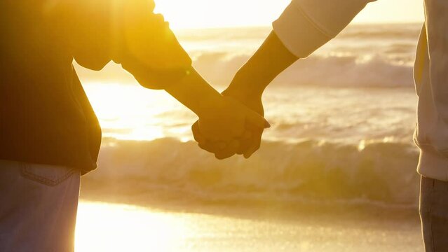 Close up of casually dressed loving young couple holding hands watching beautiful sunrise morning over beach and sea in South Africa with lens flare - shot in slow motion