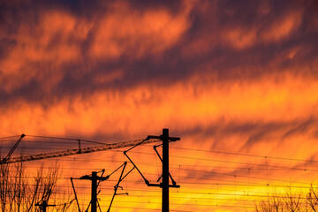 Bright red evening clouds in front of the overhead line of a railway track at sunset