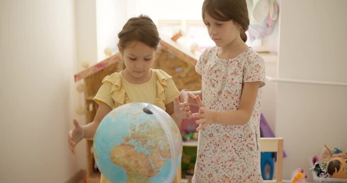 Two sisters learning geography on a world globe at home