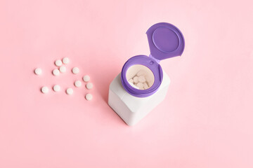 Jar with pills and scattered pills on pink background