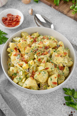 Fototapeta na wymiar Salad of potatoes, eggs, bacon and fresh herbs with mayonnaise and yogurt dressing in a bowl on a gray concrete background.