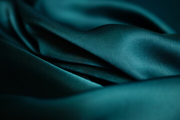 Emerald green silk or satin, draped fabric, elegant background. Beautiful wavy space for design Close-up images are blurry or blurred.